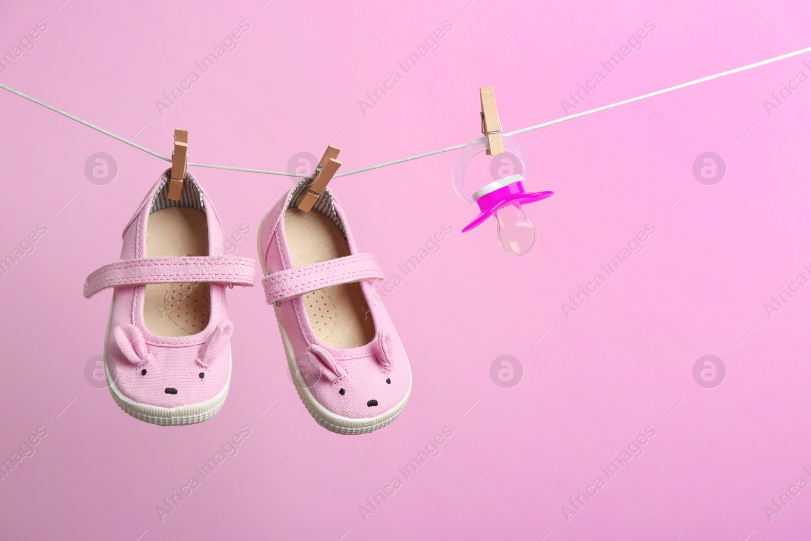 Photo of Small shoes and pacifier hanging on washing line against color background, space for text. Baby accessories