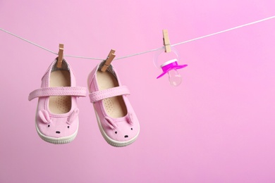 Photo of Small shoes and pacifier hanging on washing line against color background, space for text. Baby accessories