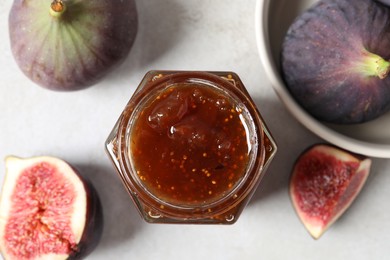 Photo of Jar of tasty sweet jam and fresh figs on white table, flat lay