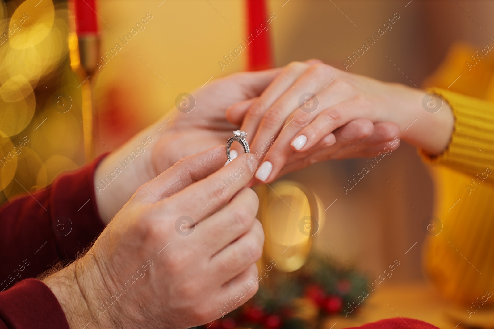 Photo of Making proposal. Man putting engagement ring on his girlfriend's finger at home on Christmas, closeup