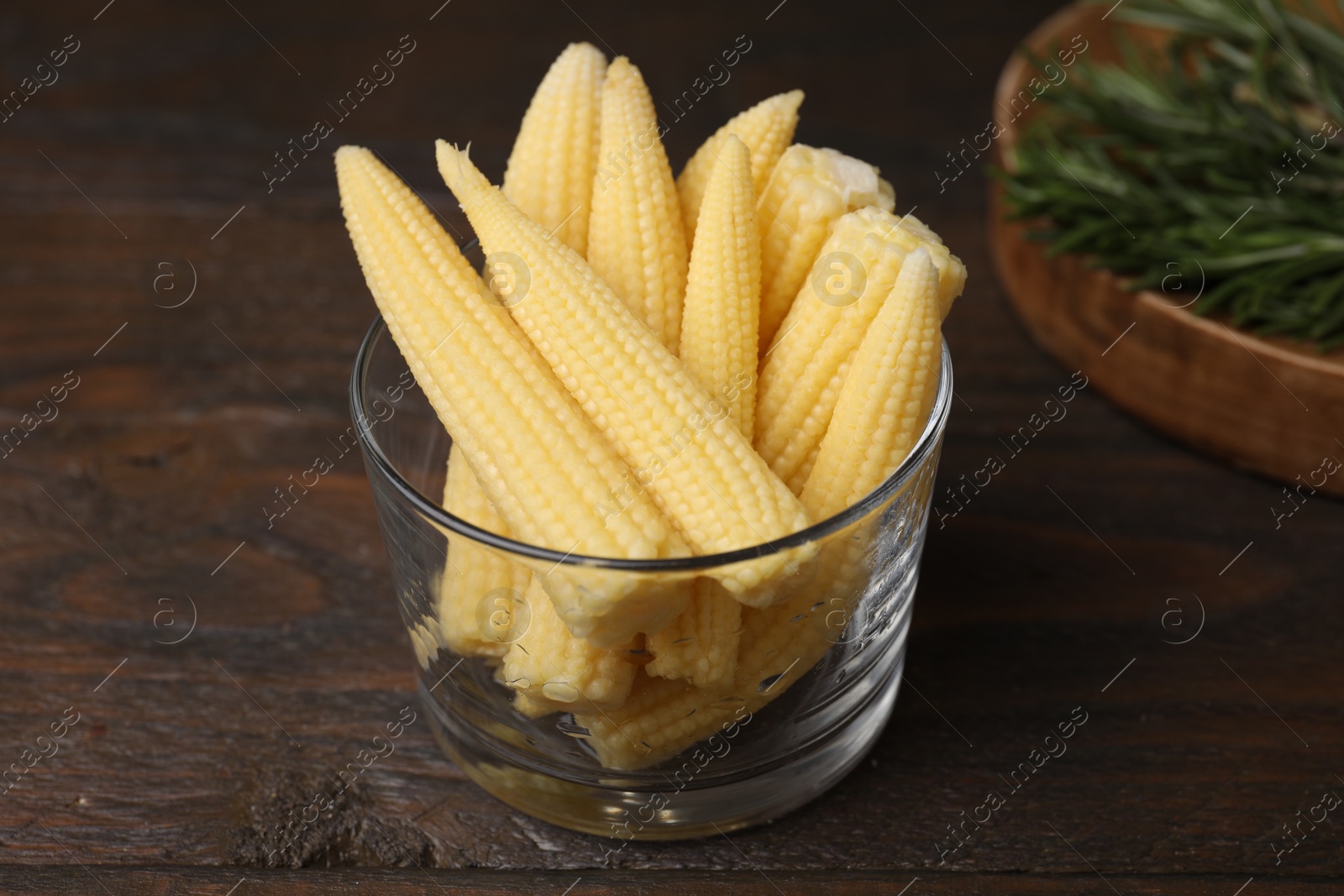 Photo of Tasty fresh yellow baby corns in glass on wooden table