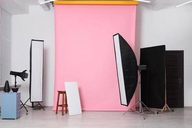 Photo of Pink photo background, stool and professional lighting equipment in studio