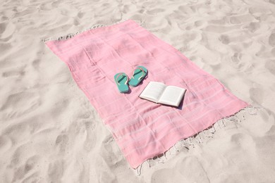 Pink striped beach towel, flip flops and book on sand