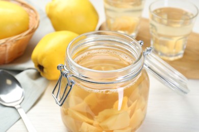 Photo of Delicious quince drink in glass jar and fresh fruits on white table, closeup