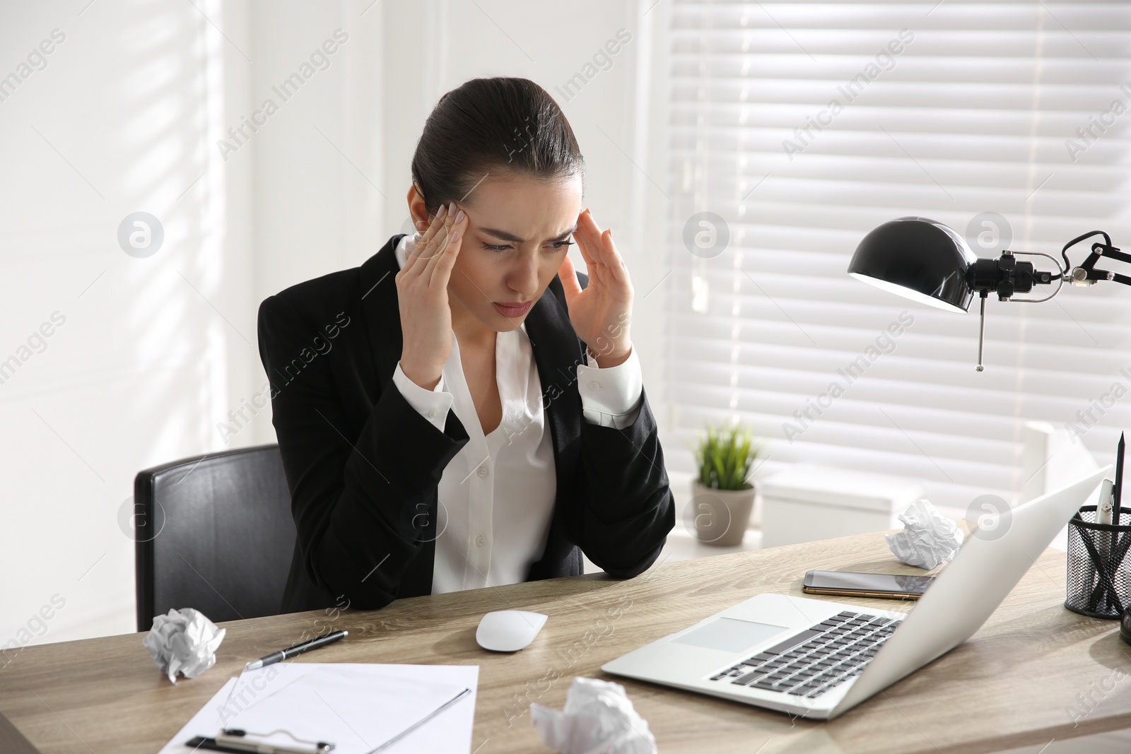 Photo of Stressed and tired young woman with headache at workplace