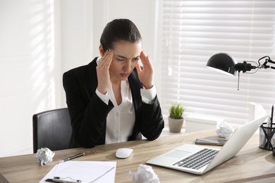 Photo of Stressed and tired young woman with headache at workplace