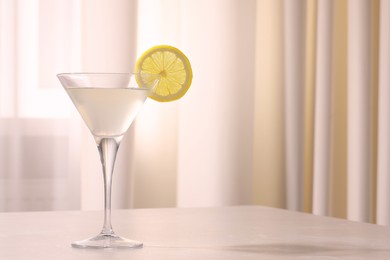 Elegant martini glass with fresh cocktail and lemon slice on beige marble table indoors. Space for text