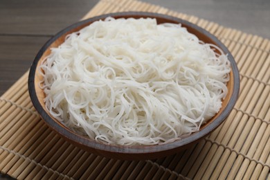 Photo of Bowl with cooked rice noodles and straw mat on table, closeup