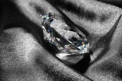 Photo of Beautiful shiny diamond on black silky fabric, closeup
