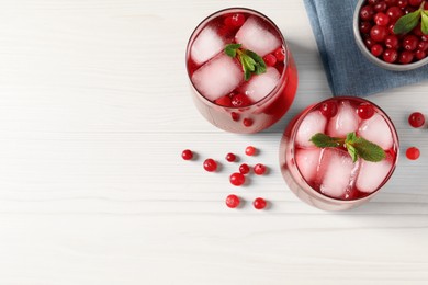 Photo of Tasty cranberry juice with ice cubes in glasses and fresh berries on white wooden table, flat lay. Space for text