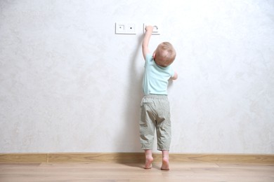 Photo of Little child playing with electrical socket indoors, back view. Dangerous situation