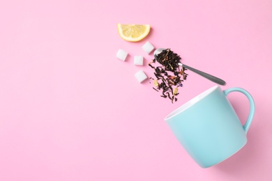 Flat lay composition with overturned cup and dry tea leaves on pink background, space for text