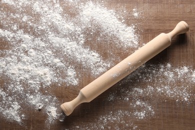 Photo of Scattered flour and rolling pin on wooden table, top view