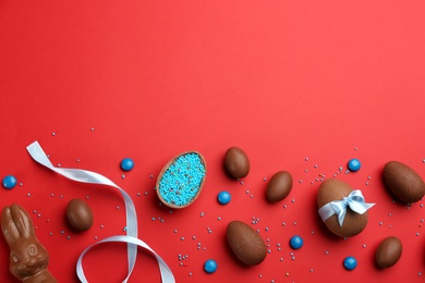 Photo of Sweet chocolate eggs and candies on red background, flat lay. Space for text