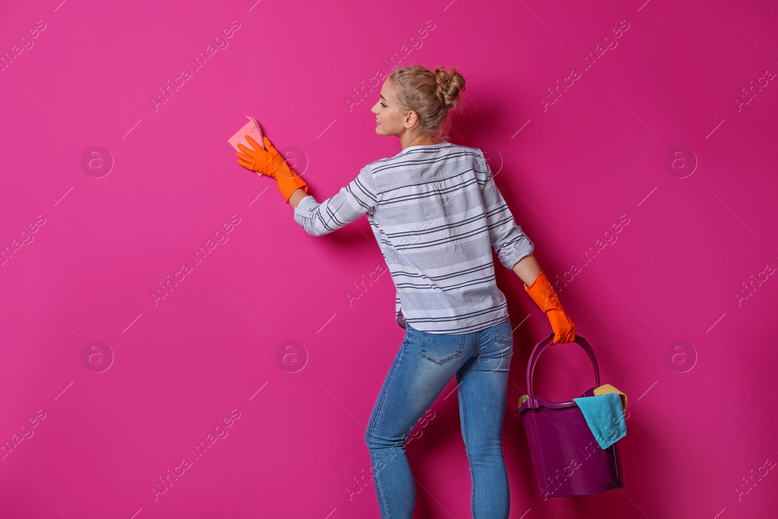 Photo of Woman in gloves cleaning color wall with rag