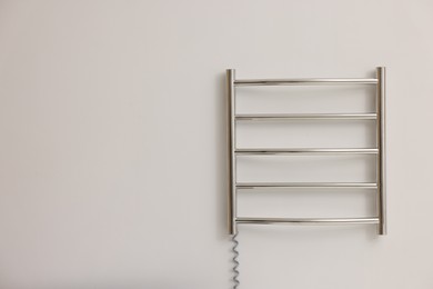 Heated towel rail on white wall, space for text