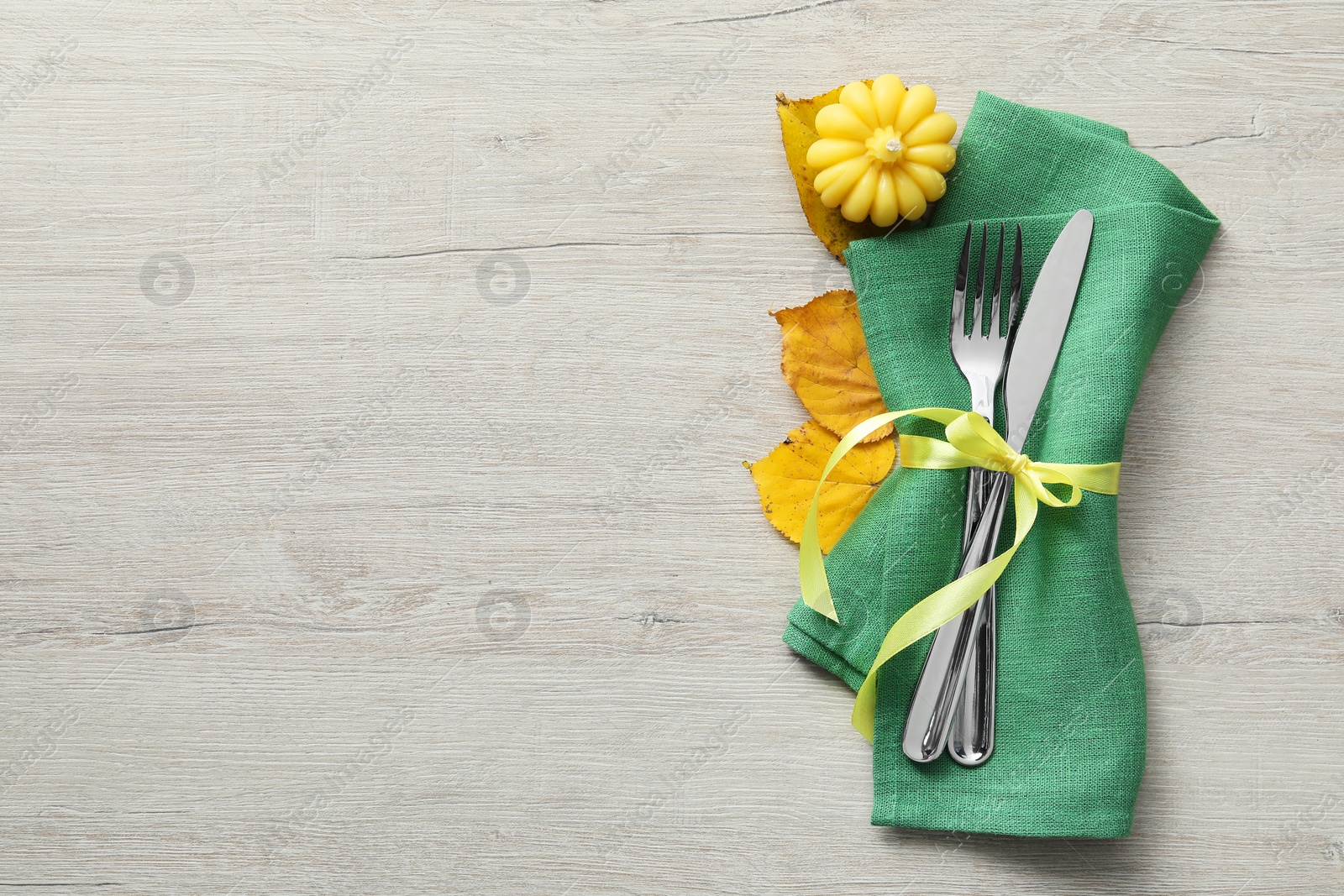 Photo of Thanksgiving table setting. Cutlery, napkin, autumn leaves and pumpkin shaped candle on light wooden background, flat lay with space for text