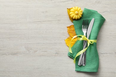 Photo of Thanksgiving table setting. Cutlery, napkin, autumn leaves and pumpkin shaped candle on light wooden background, flat lay with space for text