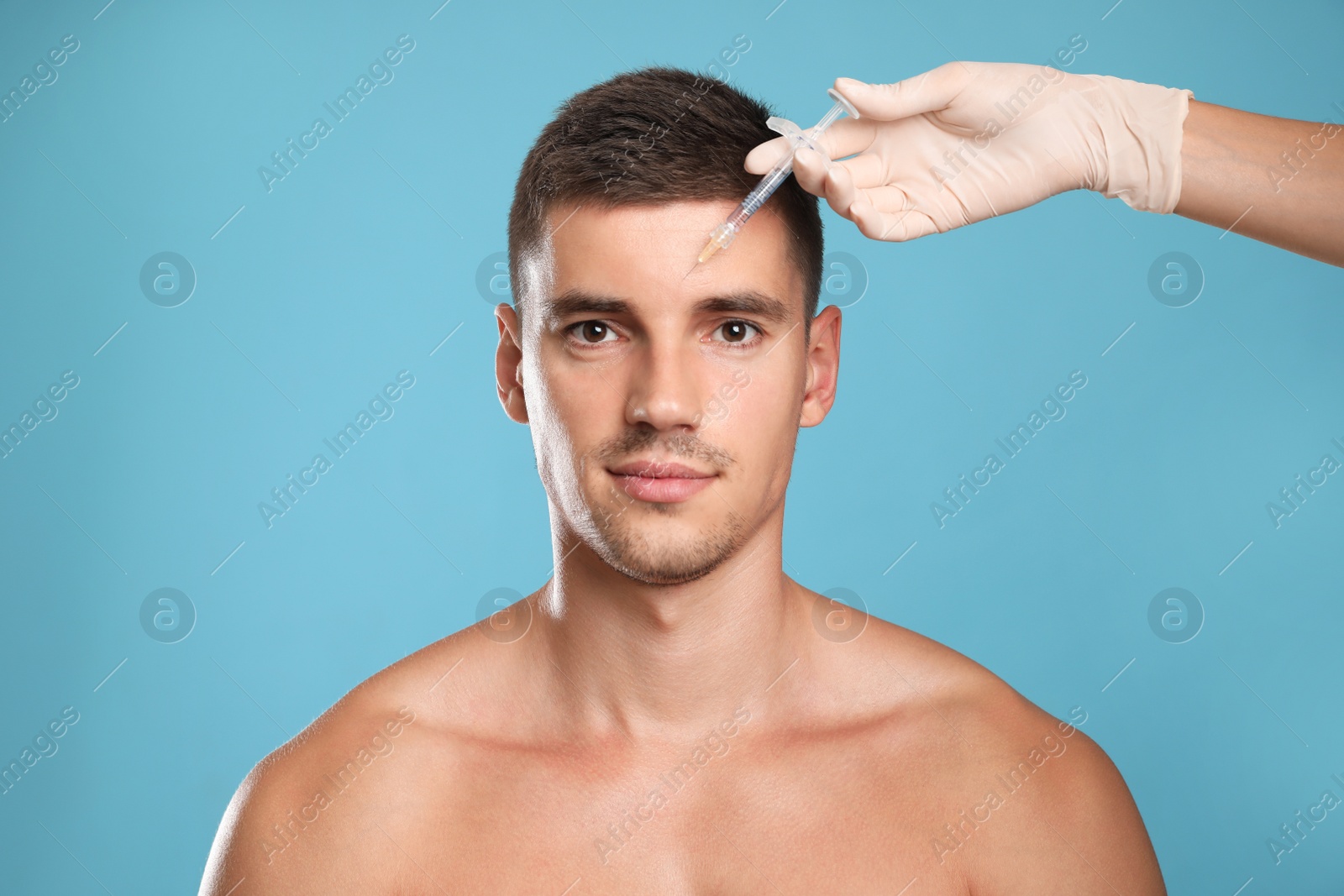 Photo of Man getting facial injection on light blue background. Cosmetic surgery