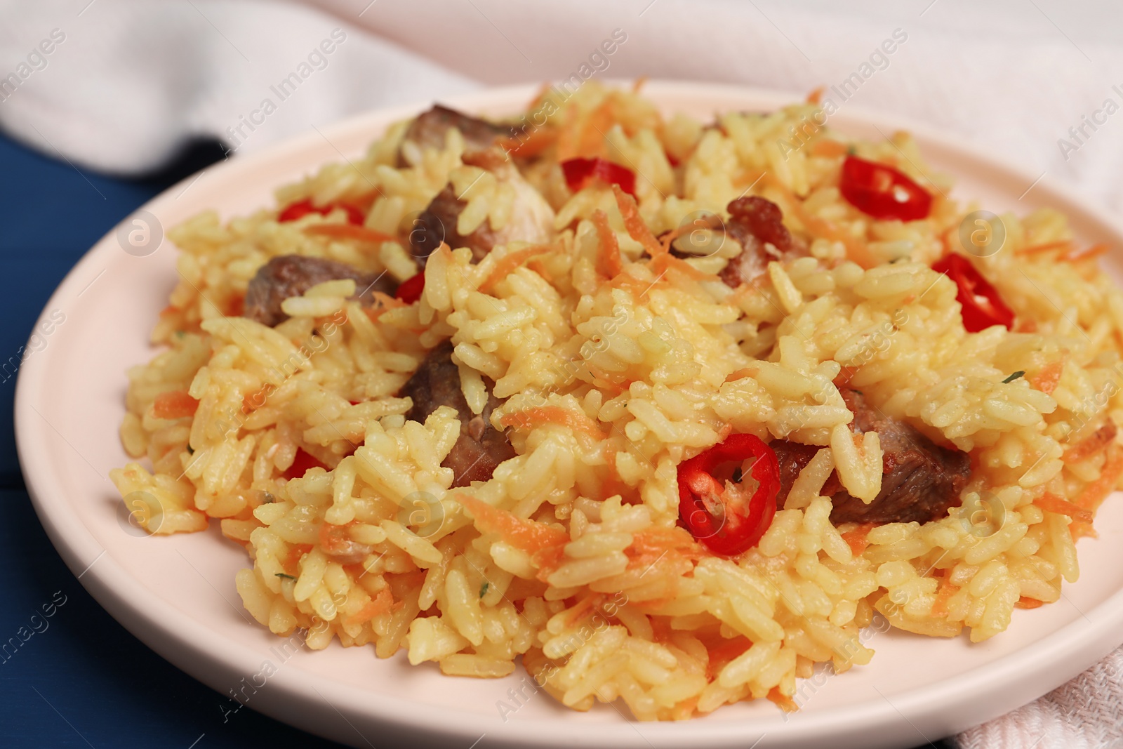 Photo of Delicious pilaf with meat on blue table, closeup