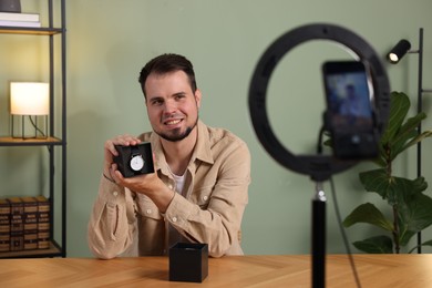 Photo of Smiling fashion blogger showing wristwatch while recording video at home