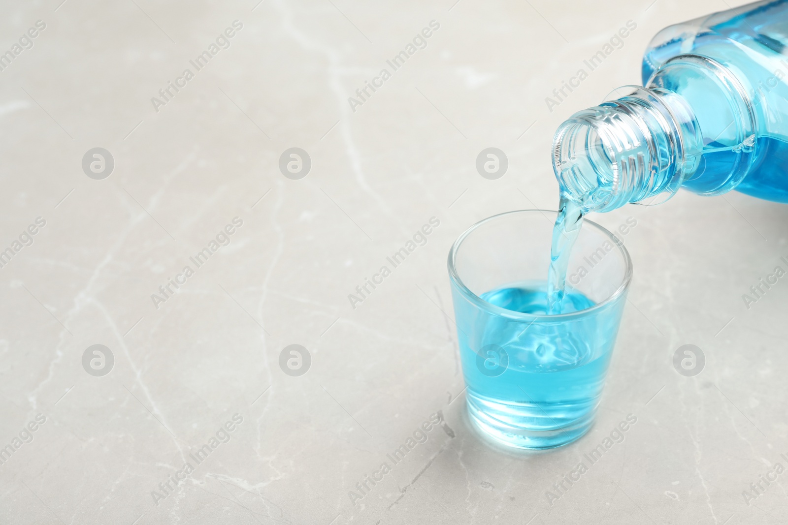 Photo of Pouring mouthwash in glass and space for text on light background. Teeth hygiene