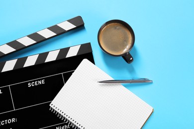 Movie clapper, coffee, notebook and pen on light blue background, flat lay