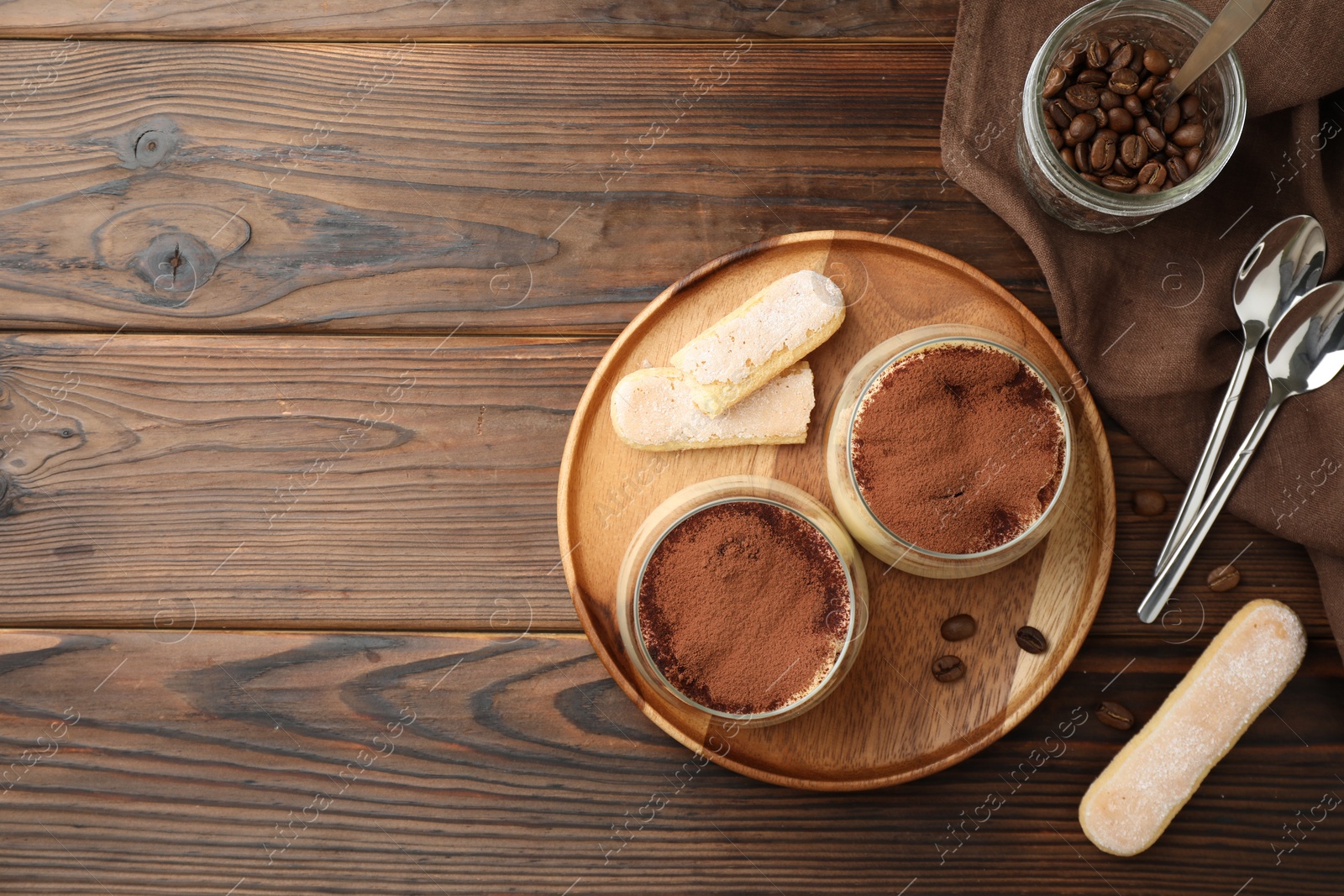 Photo of Delicious tiramisu in glasses served on wooden table, flat lay. Space for text