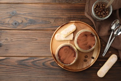 Photo of Delicious tiramisu in glasses served on wooden table, flat lay. Space for text