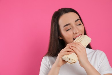 Young woman eating tasty shawarma on pink background. Space for text