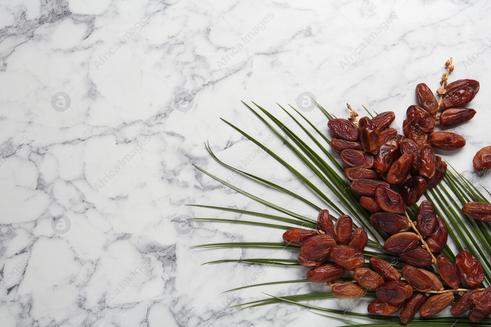 Photo of Tasty sweet dried dates and palm leaf on white marble table, flat lay. Space for text