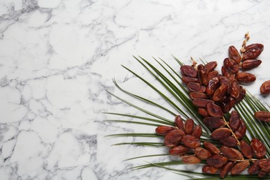 Tasty sweet dried dates and palm leaf on white marble table, flat lay. Space for text
