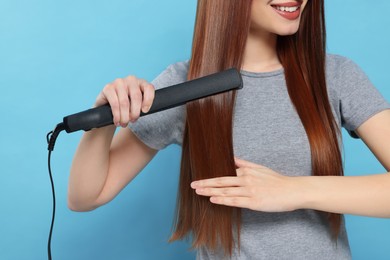 Photo of Woman using hair iron on light blue background, closeup