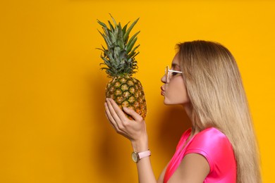 Young woman with fresh pineapple on yellow background, space for text. Exotic fruit
