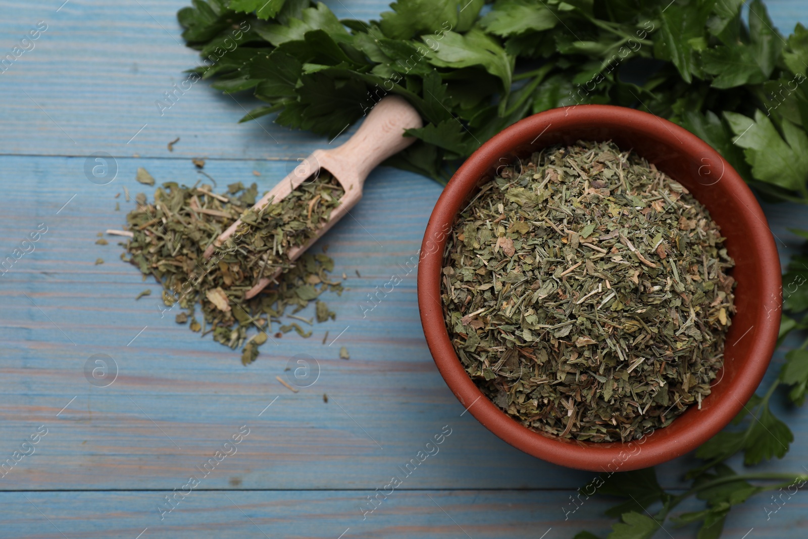 Photo of Dried parsley and fresh leaves on light blue wooden table, flat lay