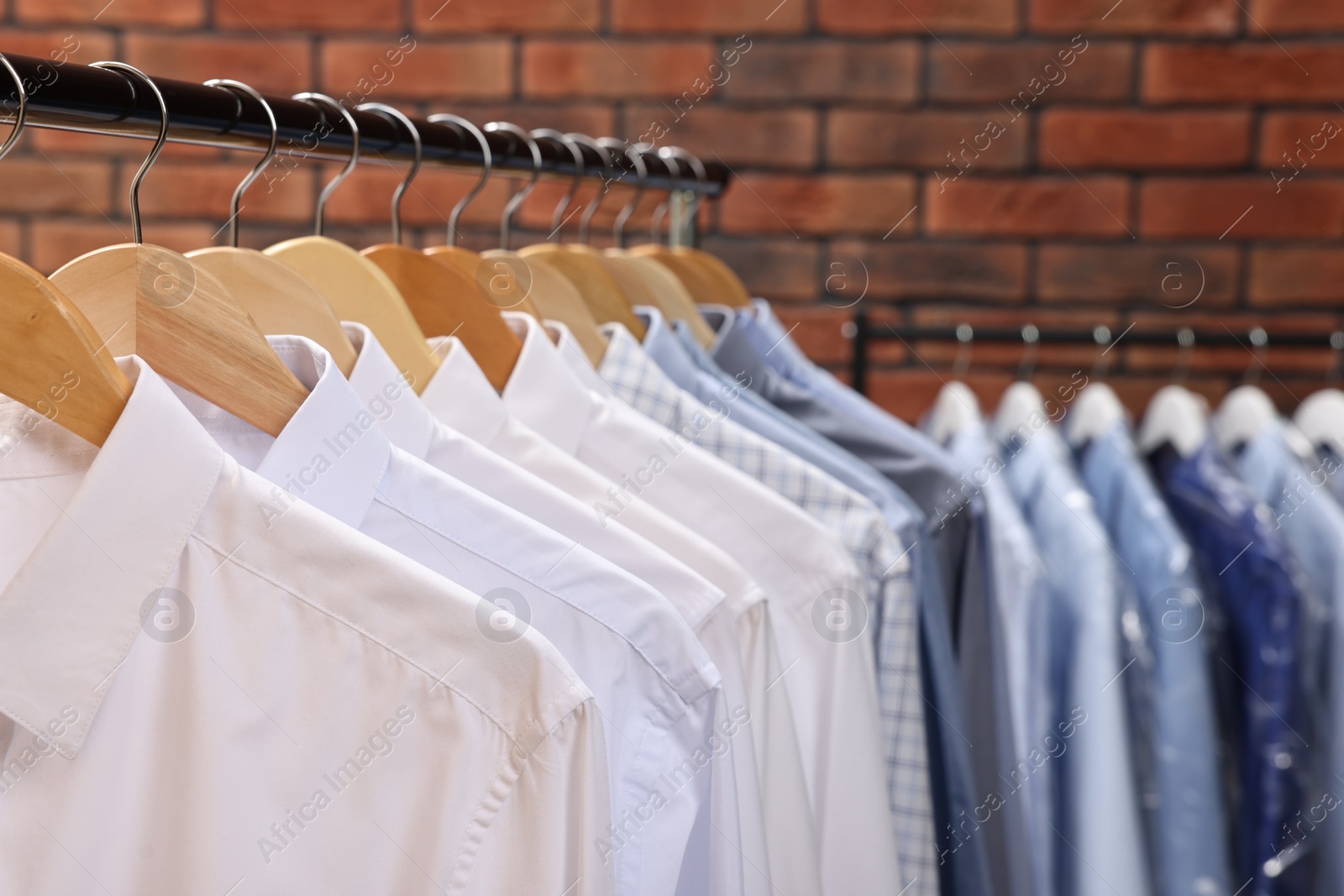 Photo of Dry-cleaning service. Many different clothes hanging on rack against brick wall, closeup