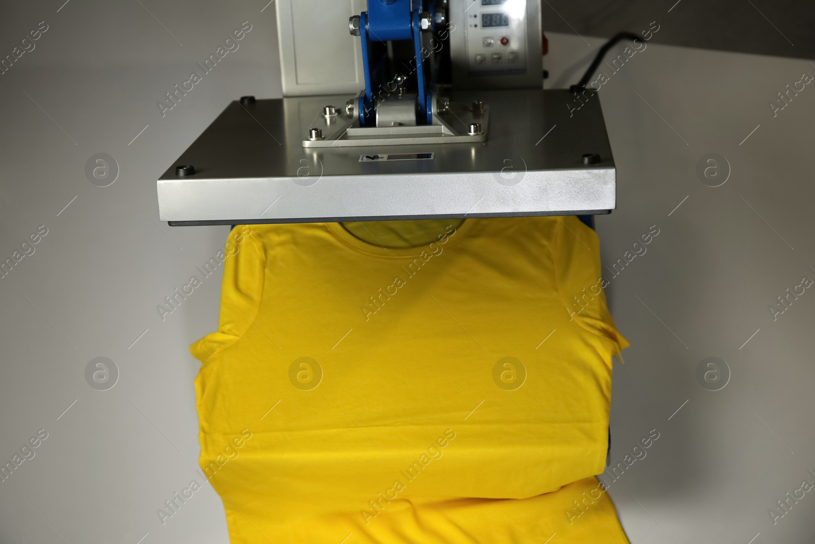 Photo of Printing logo. Heat press with yellow t-shirt on white table