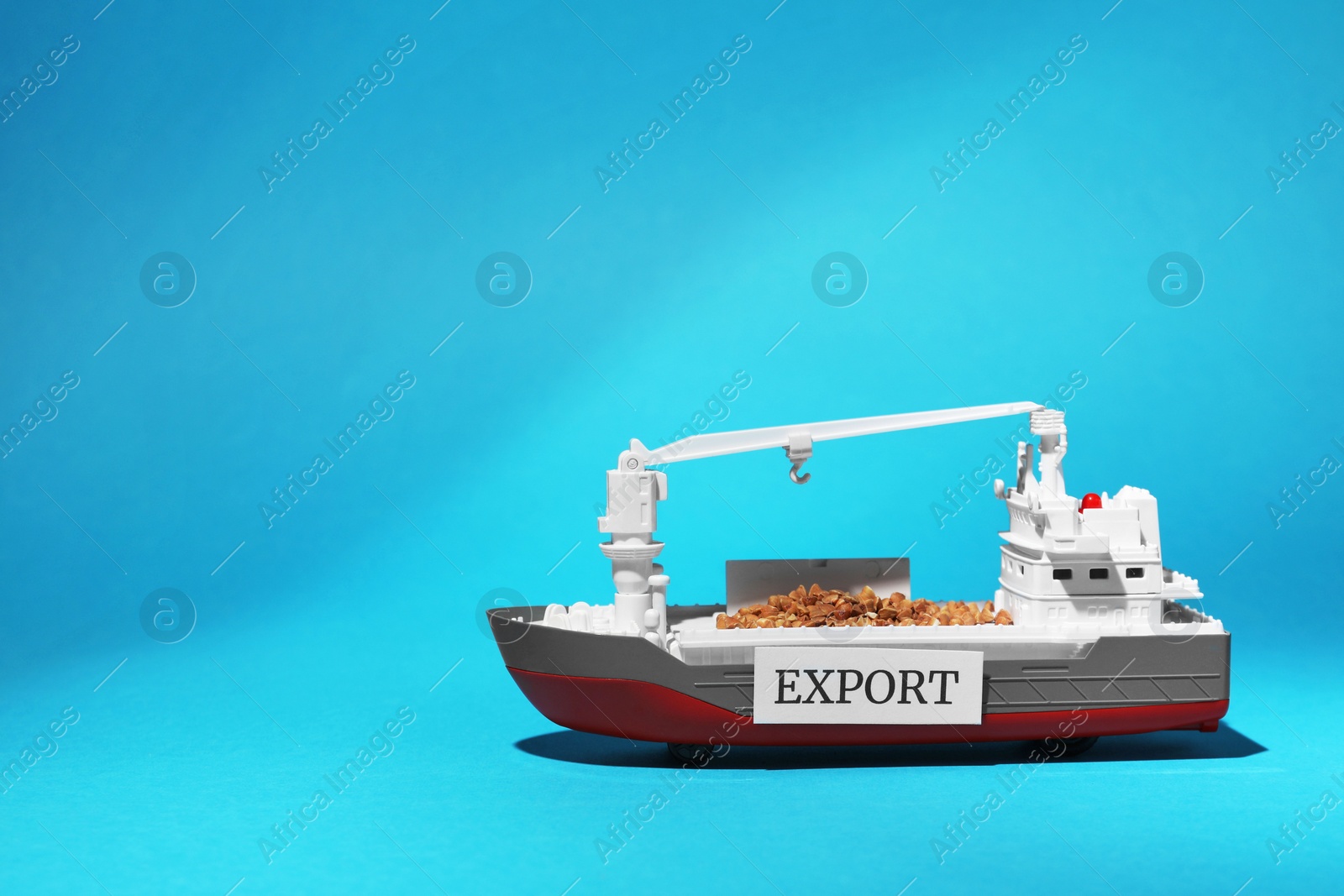 Photo of Toy cargo vessel with grains on light blue background, space for text. Export concept