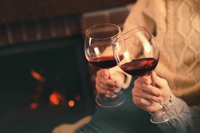 Couple with glasses of red wine near fireplace, closeup