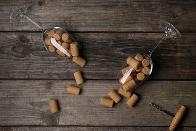 Glasses with wine corks on wooden table, flat lay