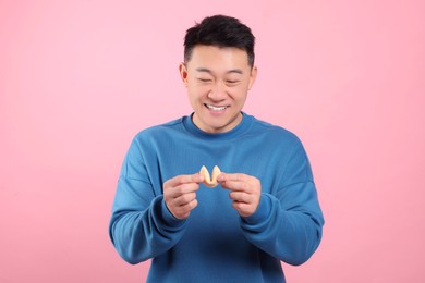 Happy asian man holding tasty fortune cookie with prediction on pink background