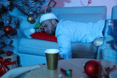 Photo of Drunk man wearing Santa hat sleeping on sofa after New Year party