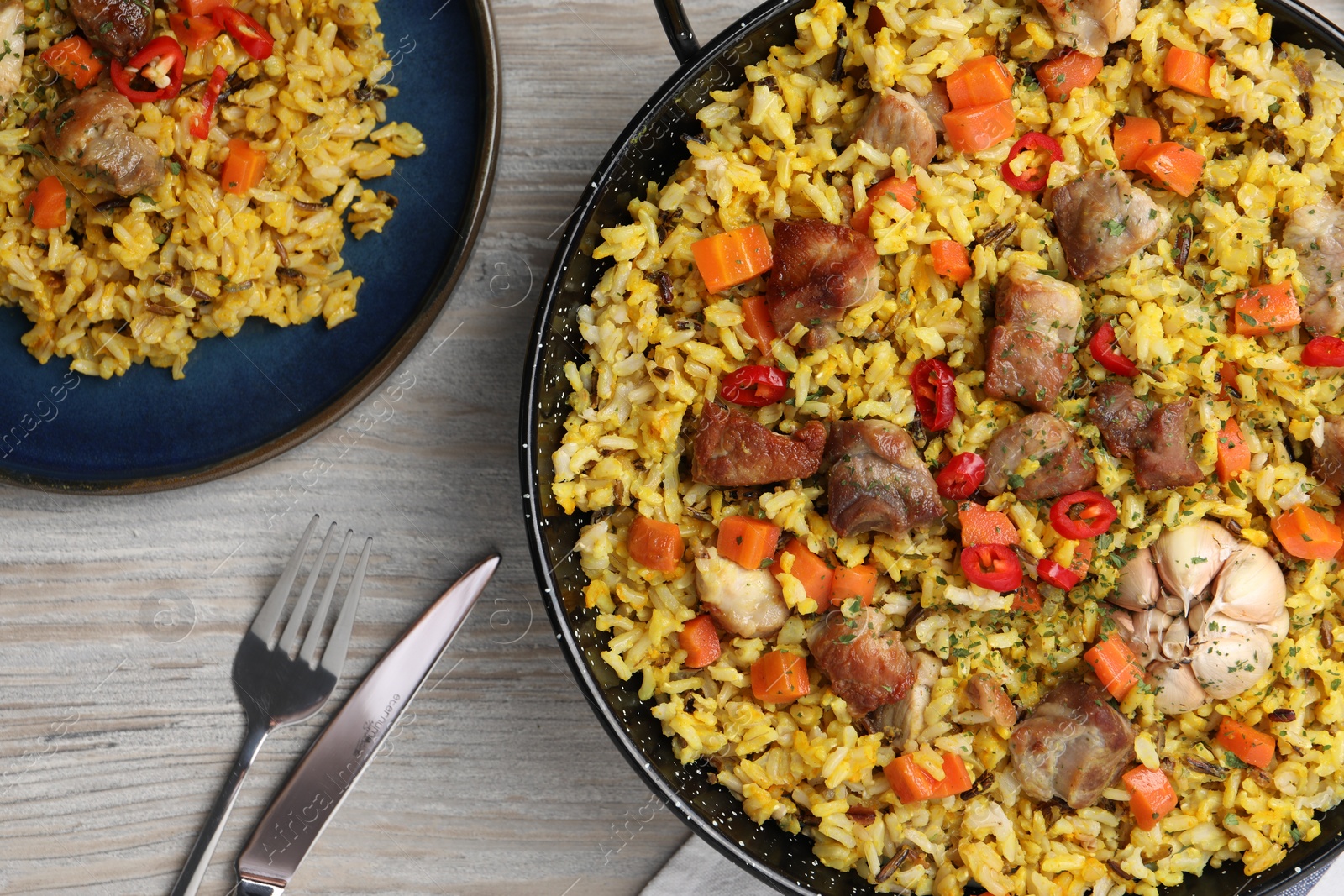 Photo of Delicious pilaf with meat, carrot and chili pepper served on wooden table, flat lay