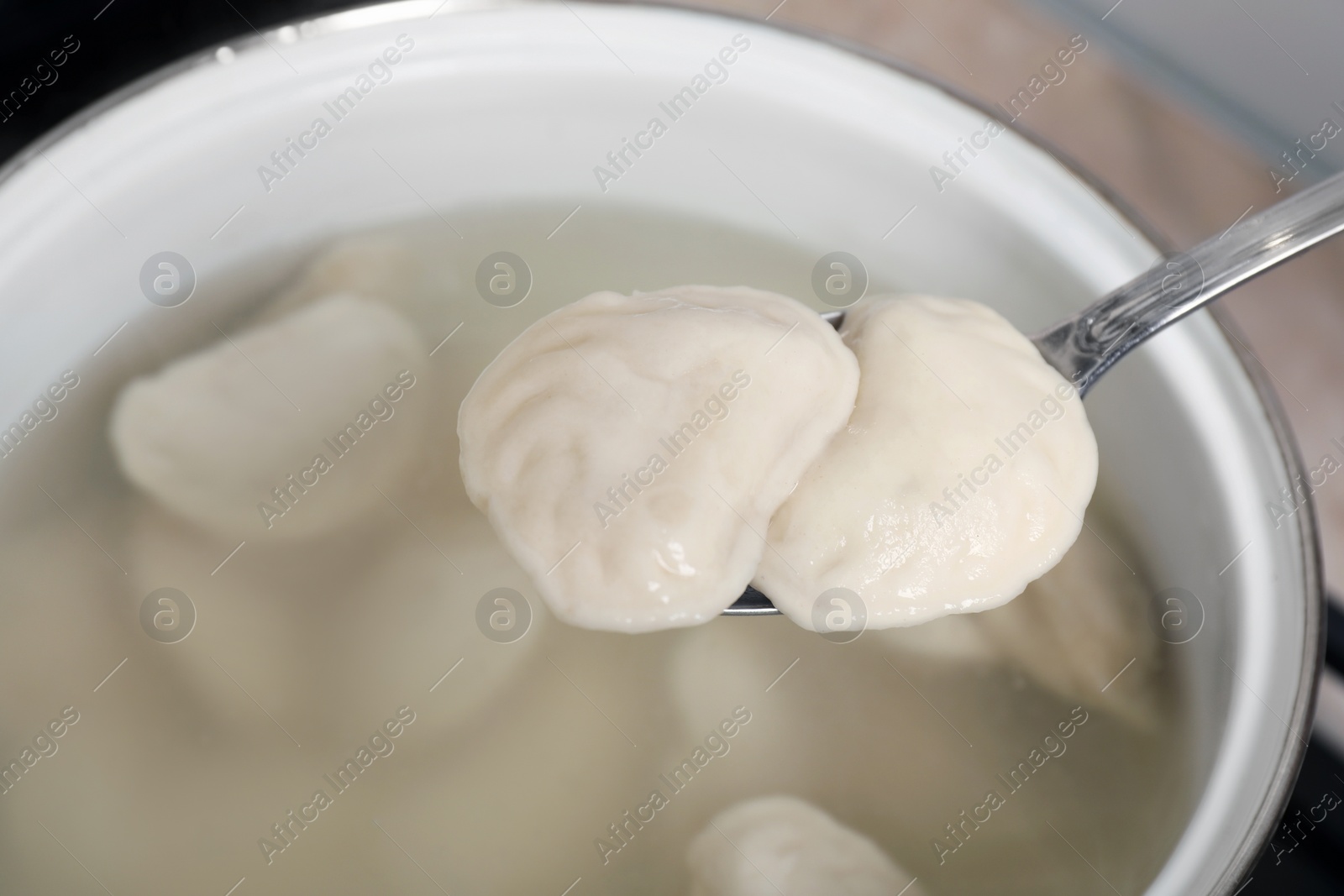 Photo of Spoon with tasty dumplings (varenyky) over pot, closeup