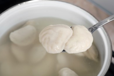 Spoon with tasty dumplings (varenyky) over pot, closeup