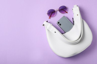 Photo of Stylish women's bag with smartphone and sunglasses on violet background, flat lay. Space for text
