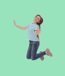 Image of Happy cute girl jumping on light turquoise background