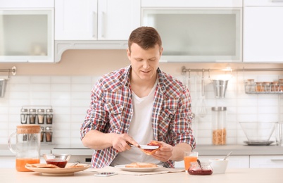 Photo of Young man spreading jam on tasty toasted bread at table in kitchen