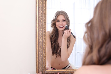 Photo of Young woman applying makeup near mirror in dressing room