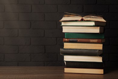 Image of Stack of old hardcover books on wooden table near brick wall, space for text